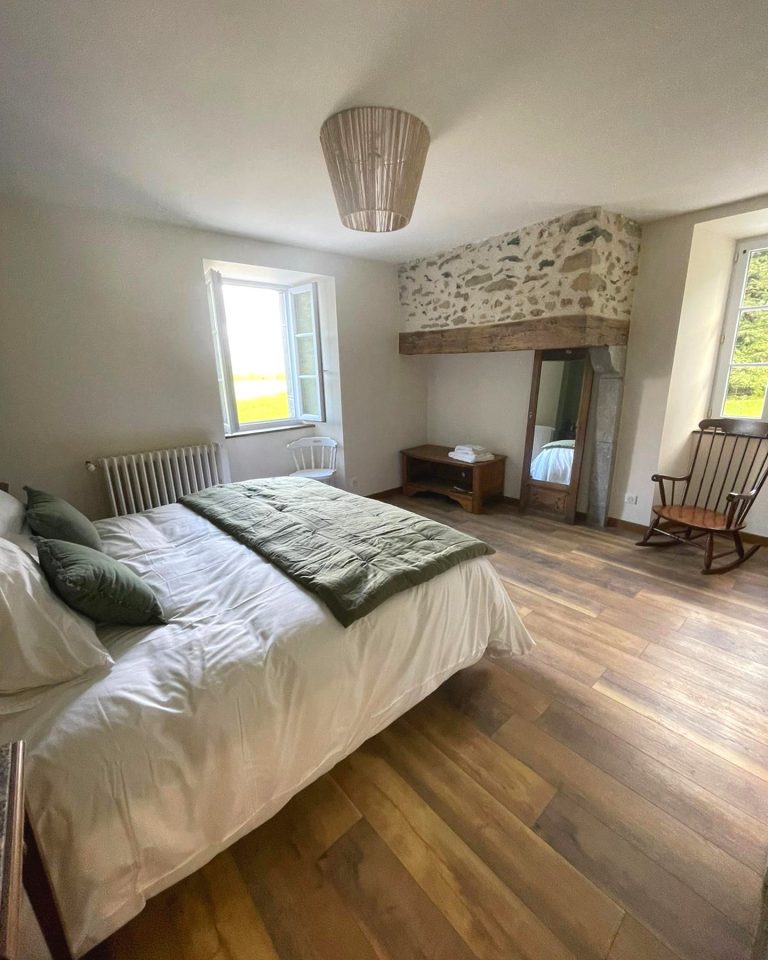 Chambre chaleureuse du Val Éveillé, literie blanche, cheminée en pierre apparente et parquet