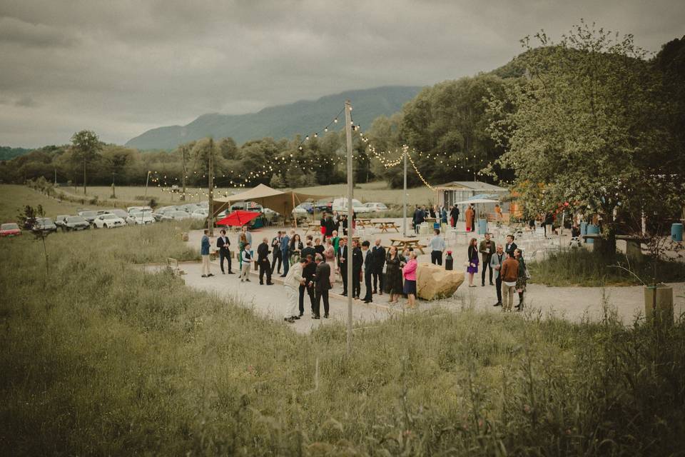 Rassemblement en extérieur dans la prairie du Val Éveillé, guirlandes lumineuses et montagnes en fond